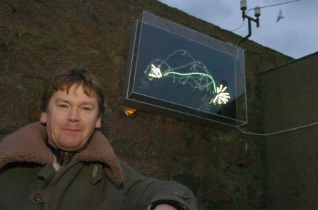 Stephen Healy in front of his animated neon sperm-whale sculpture, installed on the wall of a fishmonger's shop in Peterhead, March 2006. Photograph by Sans façon.